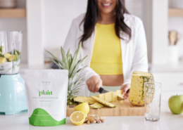 Woman preparing protein smoothie in ktichen slicing fresh pineapple